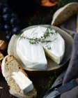 Closeup view of white cheese wheel with bread slices and grapes on wood — Stock Photo