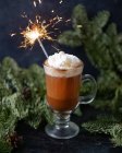 Vue rapprochée du latte dans une tasse en verre avec des branches de sapin et des branches scintillantes brûlantes — Photo de stock