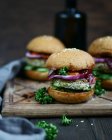 Closeup view of burgers with vegetables and sesame seeds on wooden board — Stock Photo