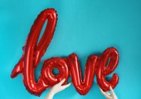 Cropped view of human hands holding air balloon in shape of love word — Stock Photo