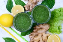 Bicchieri di spinaci con limone e zenzero frullato verde su superficie bianca con ingredienti — Foto stock