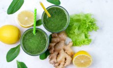 Glasses of spinach with lemon and ginger green smoothie on white surface with ingredients — Stock Photo