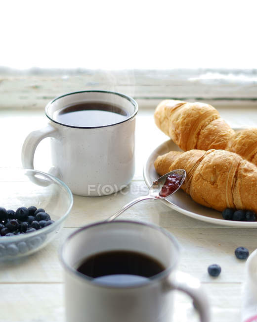 Dos tazas de té, arándanos y croissants - foto de stock