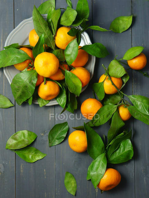 Свежие апельсины с листьями на столе — стоковое фото