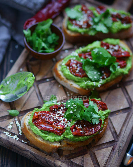 Vista de perto de sanduíches com pasta verde, salame, sementes de gergelim e salsa em tábua de madeira — Fotografia de Stock