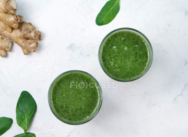 Bicchieri di spinaci e frullato verde zenzero su superficie bianca con ingredienti — Foto stock