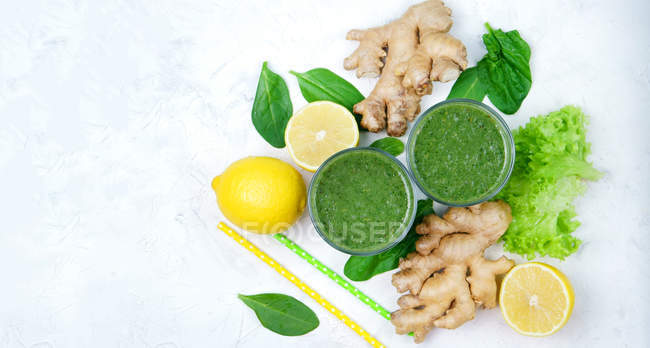 Bicchieri di spinaci con limone e zenzero frullato verde su superficie bianca con ingredienti — Foto stock