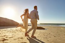 Mature couple running along beach — Stock Photo