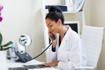 Médico en el escritorio haciendo una llamada telefónica - foto de stock