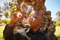 Хлопчик дме бульбашки в парку — стокове фото