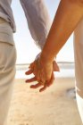 Зрелая пара, держащаяся за руки на пляже — стоковое фото