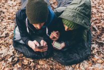 Couple couché dans des sacs de couchage regardant les smartphones — Photo de stock