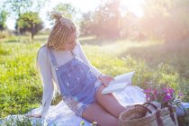 Frau liest Buch auf Picknickdecke im Feld — Stockfoto