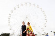Couple strolling arm in arm by ferris wheel — Stock Photo