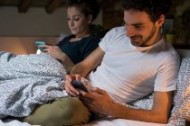 Пара сидящих в постели и смотрящих на смартфоны — стоковое фото