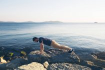 Man doing push ups on rocks by sea — Stock Photo