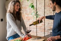 Paar schenkt Rotwein an Küchentisch ein — Stockfoto