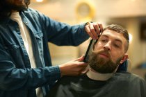 Cabeleireiro na barbearia aparando barba — Fotografia de Stock