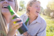 Пара, сидящая в поле и пьющая пиво в бутылках — стоковое фото