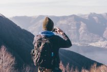Senderista masculino fotografiando lago y montañas - foto de stock