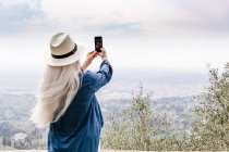 Woman with long grey hair photographing view — Stock Photo