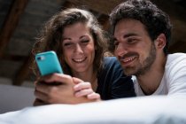 Paar liegt im Bett und schaut aufs Smartphone — Stockfoto
