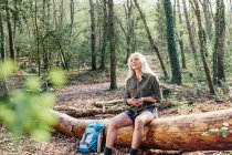 Female backpacker sitting on log in forest — Stock Photo