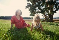 Mujer embarazada sentada en el campo con su hija - foto de stock