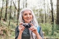 Женщина с седыми волосами фотографирует в лесу — стоковое фото