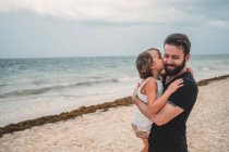 Preteen daughter kissing father at seaside — Stock Photo