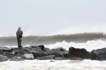 Homme pêchant dans les rochers dans les vagues orageuses de l'océan, Long Beach, New York, États-Unis — Photo de stock
