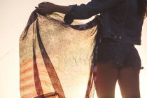 Женщина в джинсовых шортах, держит американский флаг, средняя часть, вид сзади — стоковое фото