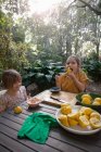 Dos hermanas jóvenes degustando y preparando limones para la limonada en la mesa del jardín - foto de stock