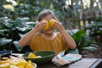 Дівчина тримає лимони на очах за садовим столом — стокове фото