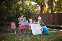 Мальчик и сестра готовят лимонад знак стенд в саду — стоковое фото