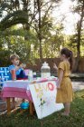 Girl buying lemonade from lemonade stand in garden — Stock Photo