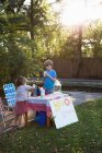 Boy and sister drinking lemonade from lemonade stand in garden — Stock Photo