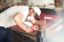 Man working with polishing machine in boat repair workshop — Stock Photo