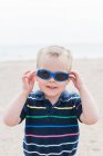 Niño pequeño que se pone gafas de sol azules - foto de stock