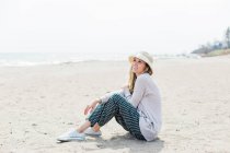 Donna in cappello da sole seduta sulla spiaggia — Foto stock