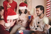 Молодые женщины и мужчины смотрят на смартфон на диване на рождественской вечеринке — стоковое фото