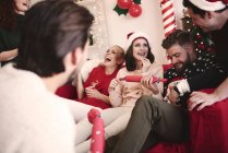 Молодые взрослые друзья тянут рождественские крекеры на диване на рождественской вечеринке — стоковое фото