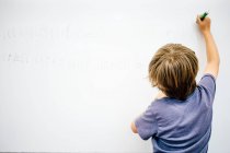 Jeune garçon écrit sur le tableau blanc — Photo de stock