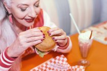 Mulher madura comer hambúrguer — Fotografia de Stock