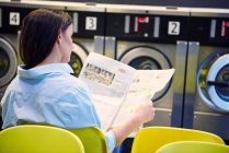 Woman reading newspaper in laundrette — Stock Photo
