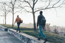 Hipster maschi che camminano lungo il muro del parco — Foto stock