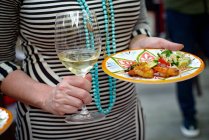 Woman holding glass of wine and plate of food — Stock Photo