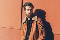 Bearded man leaning against orange wall — Stock Photo
