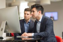 Business men looking at office desktop — стоковое фото