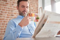 Man reading newspaper drinking coffee — Stock Photo